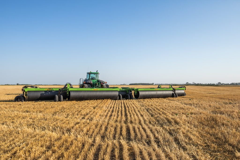 Aerial view of a green tractor pulling a Mandako 5-Plex land roller across a lush field, demonstrating its extensive coverage.